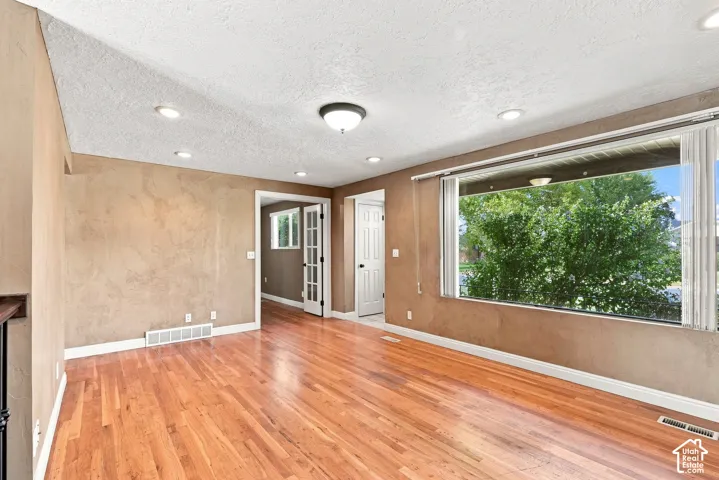 Hardwood flooring, recessed lighting, large window with blinds, ceiling-mounted light fixture, and white trim throughout