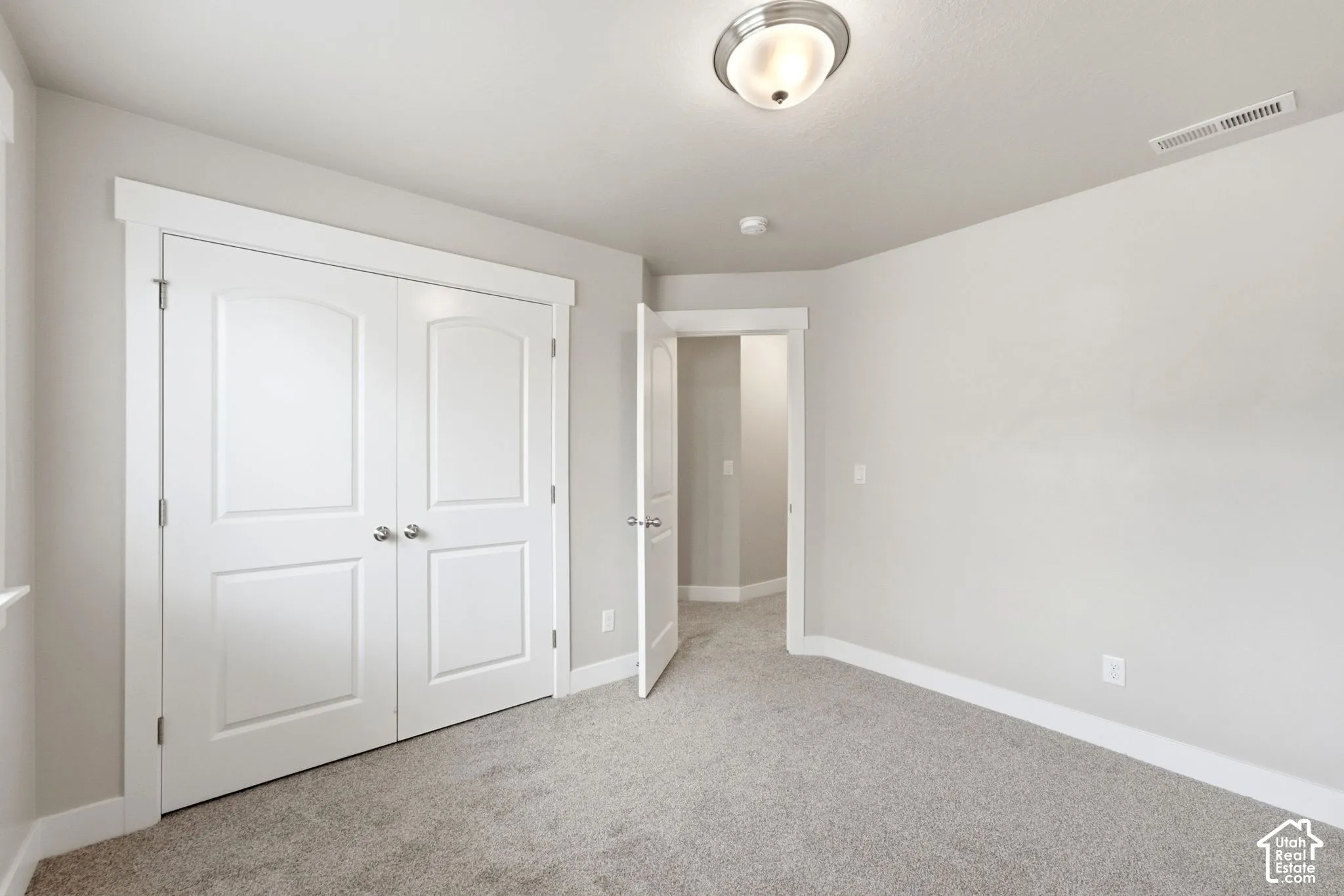 Textured carpeting, neutral wall color, white trim, flush mount ceiling light, and panel doors