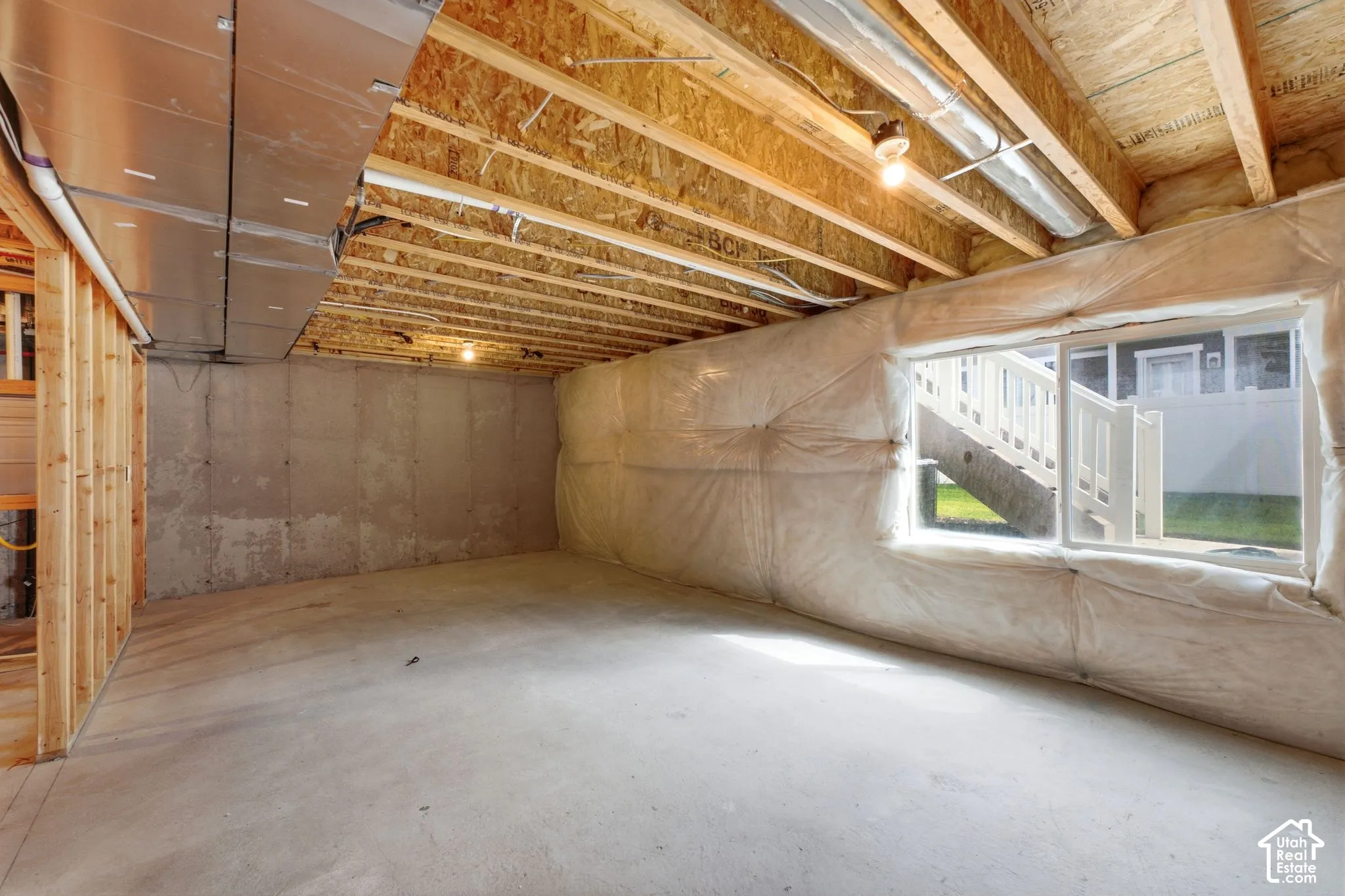 Unfinished basement featuring exposed wood joists, concrete flooring, a framed wall, and a window opening