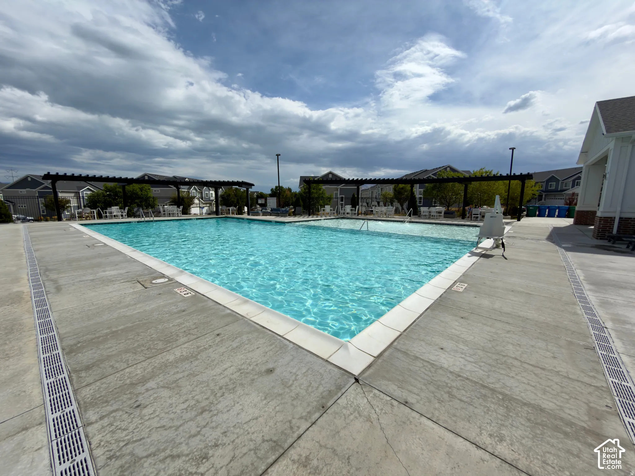Expansive outdoor pool with concrete decking, perimeter drainage, and multiple pergolas providing shaded seating areas