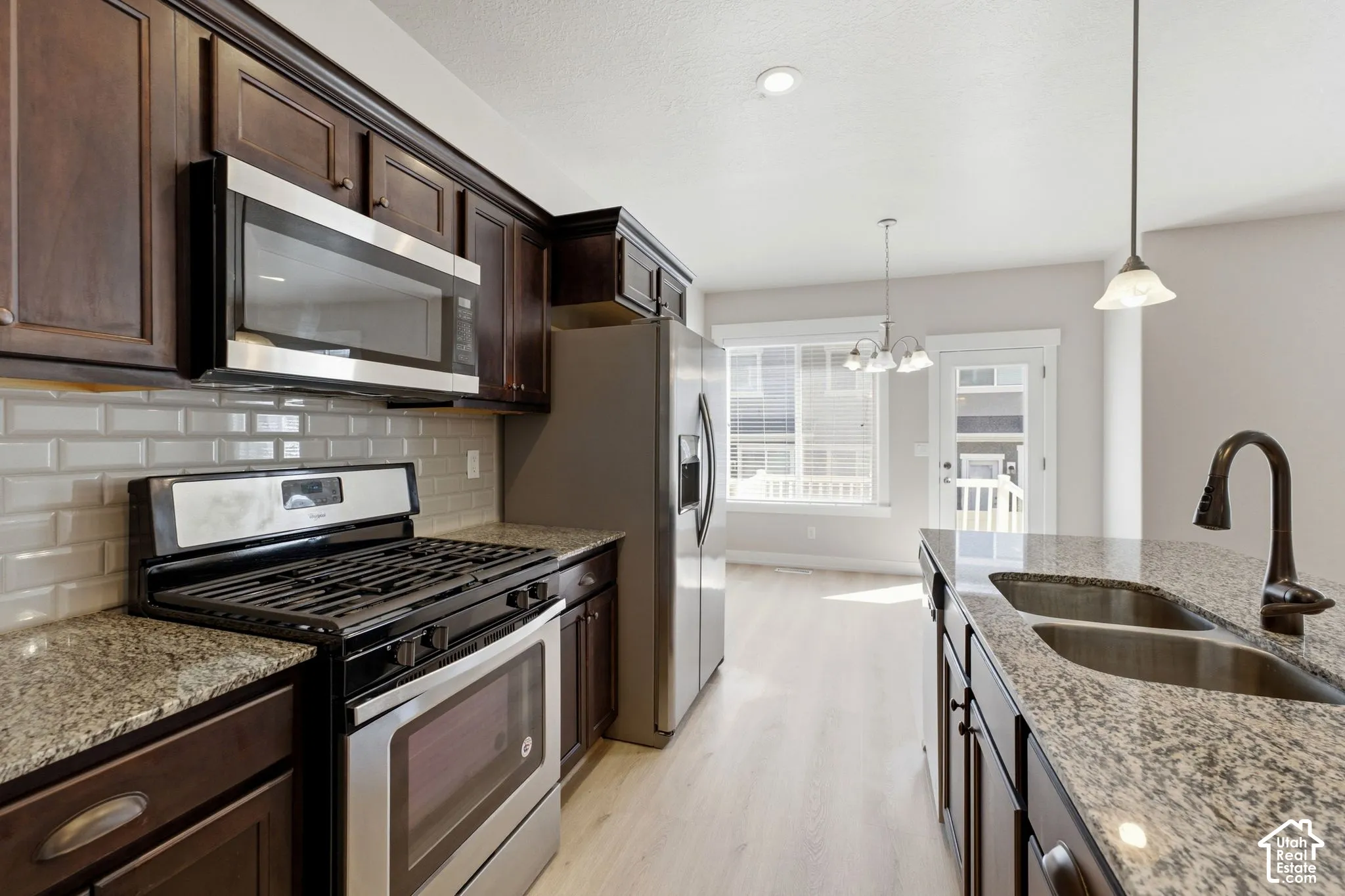 Granite countertops, stainless steel appliances, dark wood cabinetry, subway tile backsplash, and a double basin sink