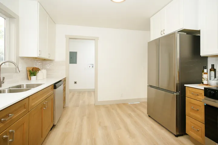 Modern kitchen featuring wood-finish flooring, stainless steel appliances, white cabinetry, a dual-basin sink, and light-toned countertops