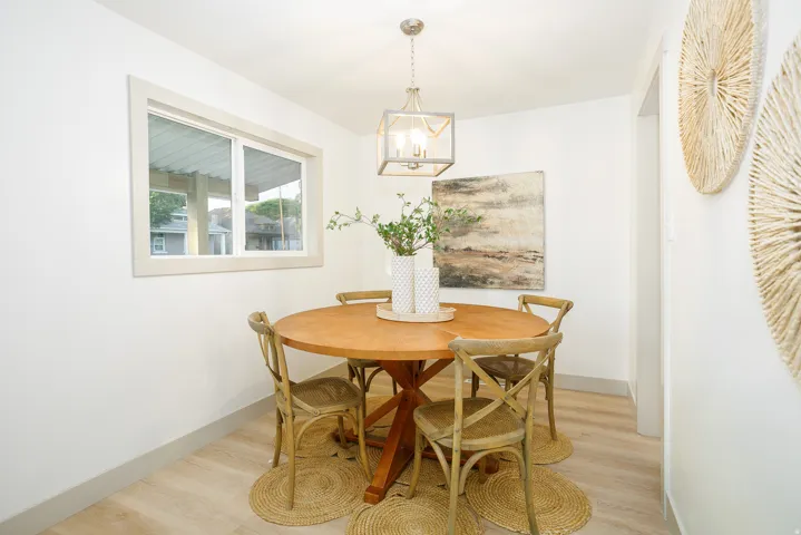 Bright dining area with wood-finish round table, natural light from multi-pane window, pendant lighting fixture, wood-finish flooring, and woven natural fiber area rug anchoring the space