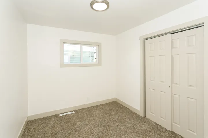 Neutral wall paint, carpet flooring, window with blinds, bi-fold closet doors, and flush mount lighting