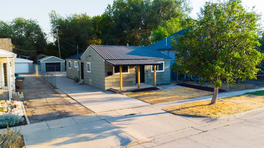 Green siding exterior with a dark metal roof, a covered entry with wood posts, and a paved driveway