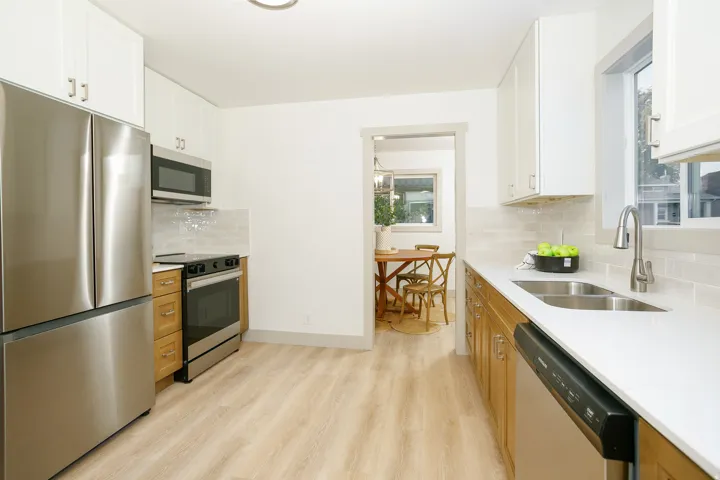 Light wood-finish flooring, white upper cabinetry, natural wood lower cabinetry, stainless steel appliances, and a double basin sink