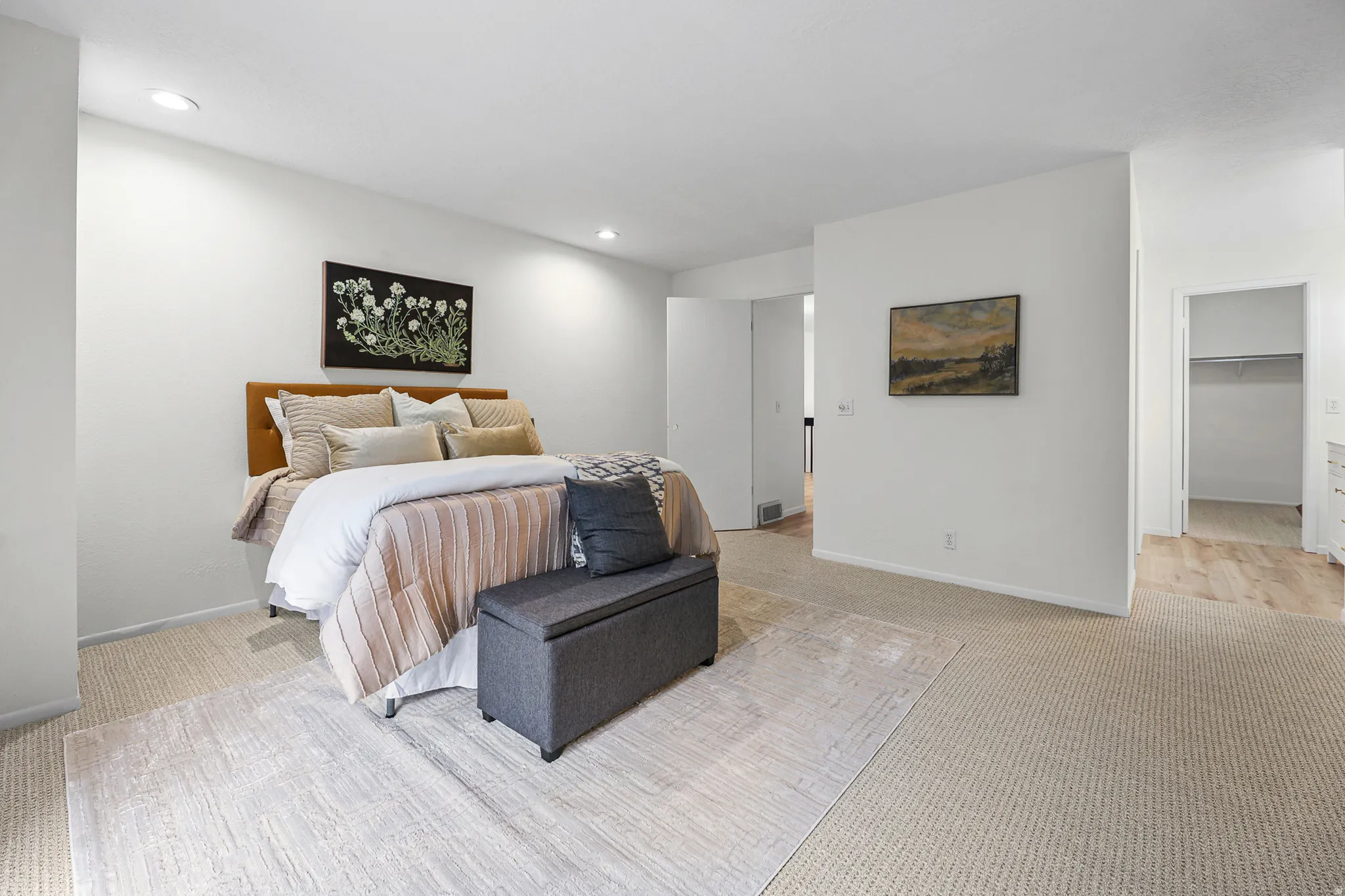 Spacious primary bedroom featuring a wood-finish headboard, recessed ceiling lighting, and direct access to a walk-in closet