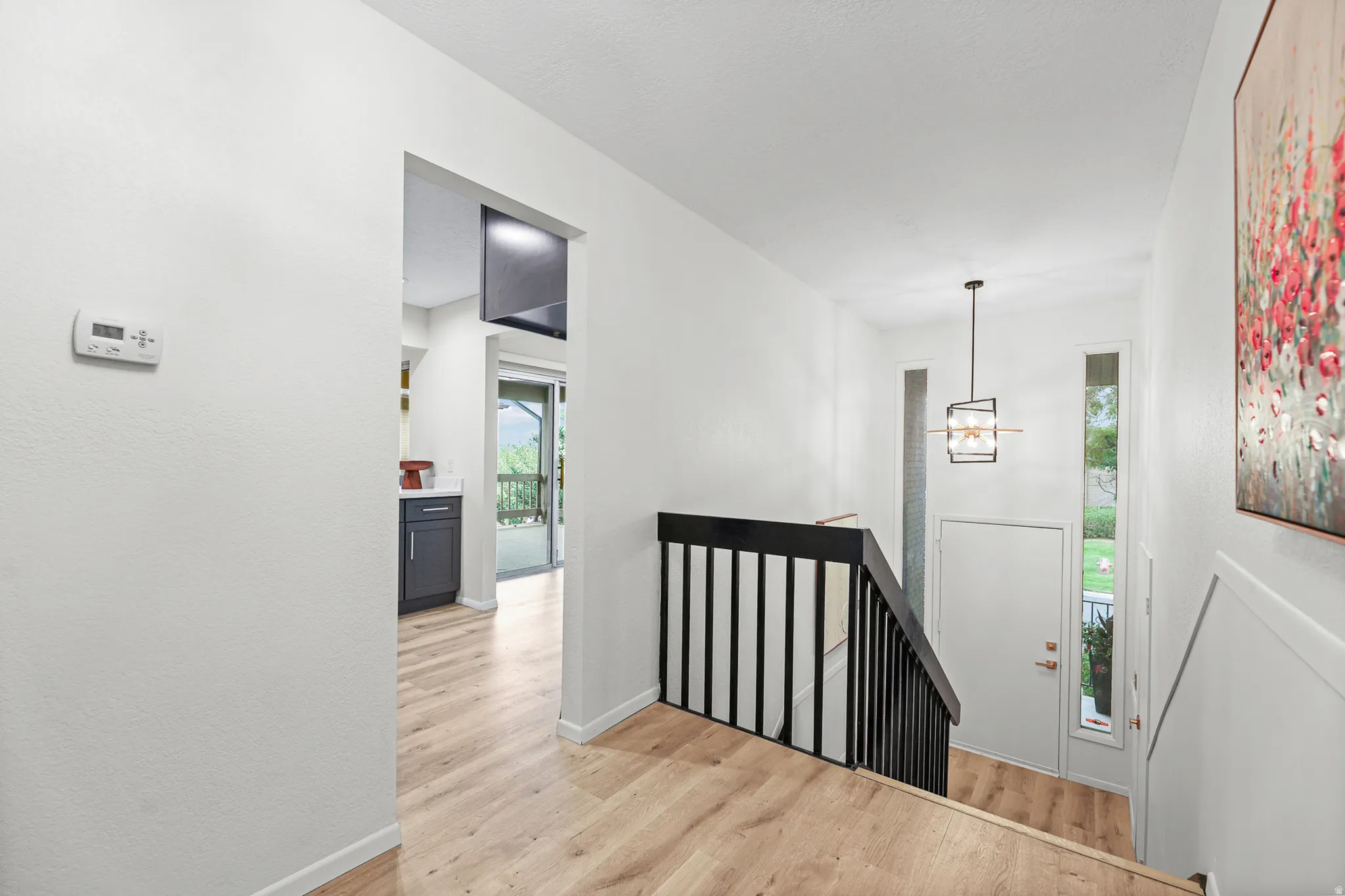Wood-finish flooring, staircase with black railing, modern pendant light fixture, and transom window beside the entry door