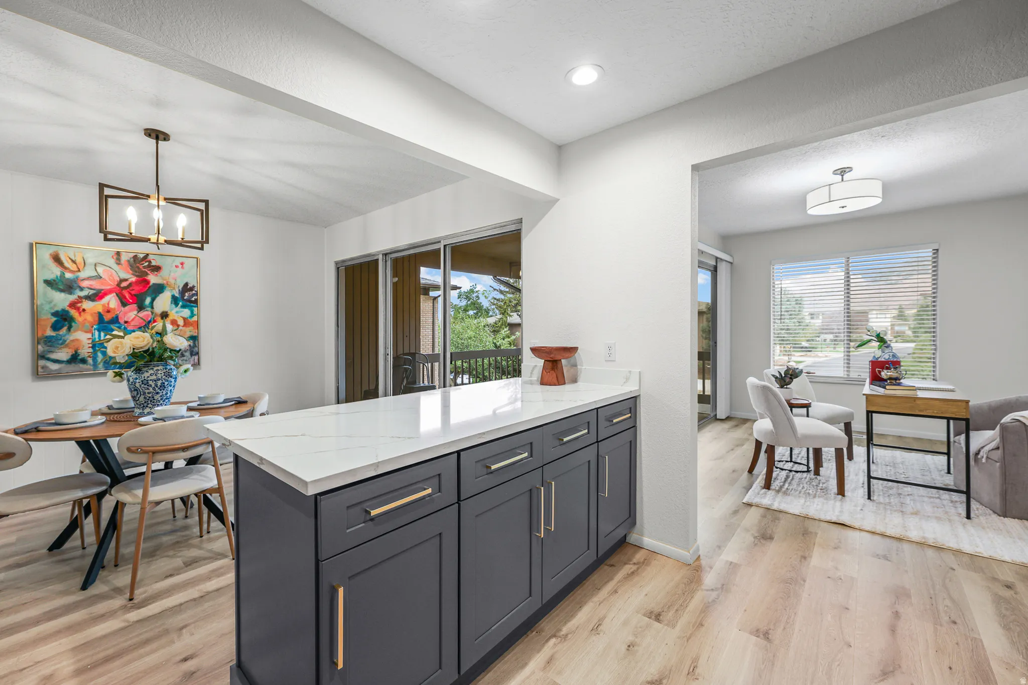 Kitchen island with a white countertop and dark cabinetry, wood-finish flooring, recessed lighting, and a dining area with a modern chandelier