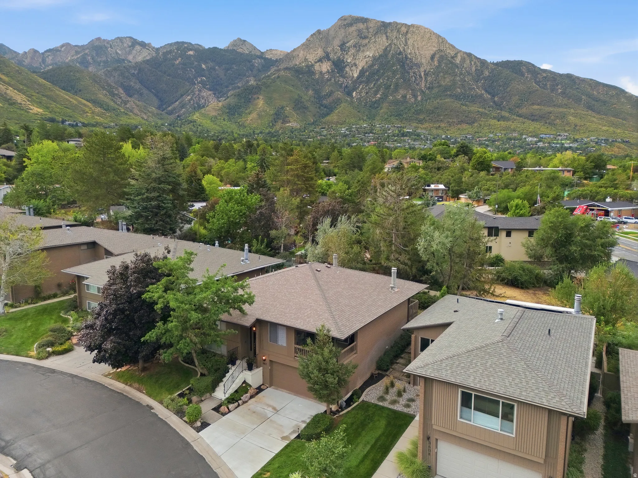 Mountain backdrop, landscaped front yard, concrete driveway, attached garage, and pitched shingle roof