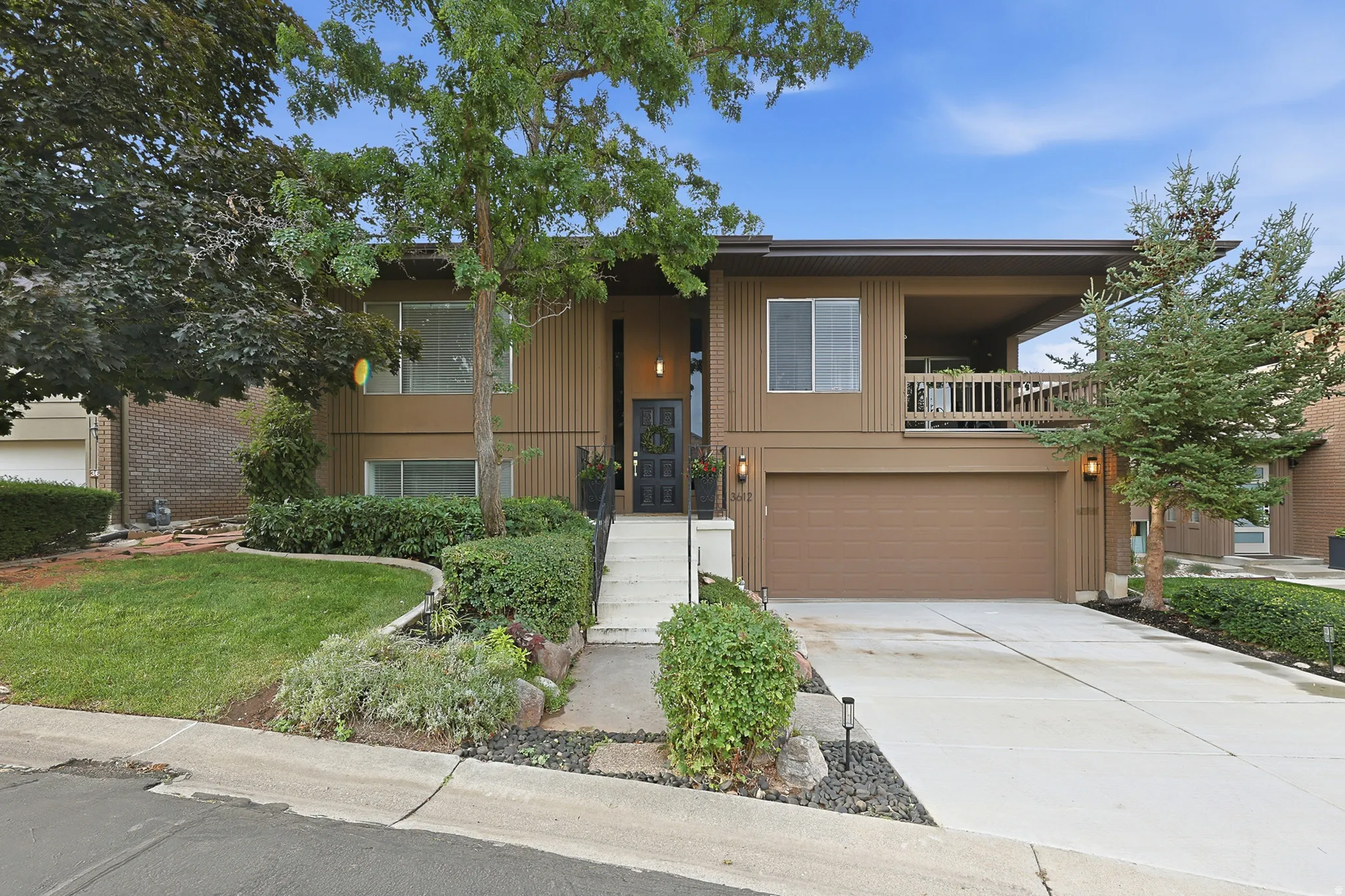 Split-level exterior with panel siding, an attached garage, a covered balcony, and mature landscaping
