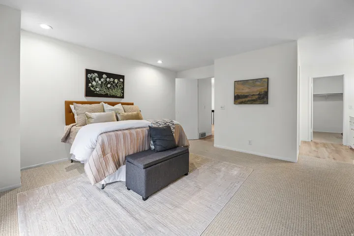 Spacious primary bedroom featuring a wood-finish headboard, recessed ceiling lighting, and direct access to a walk-in closet