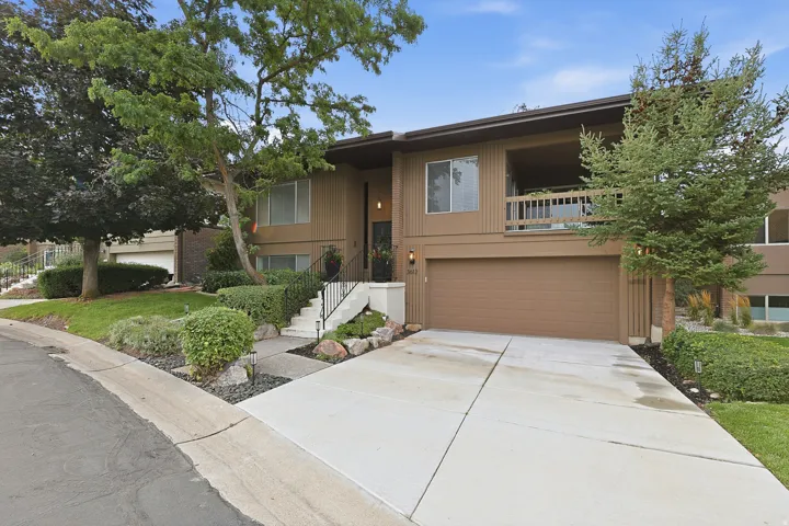Split-level residence featuring a two-car garage, upper-level balcony, and established landscaping