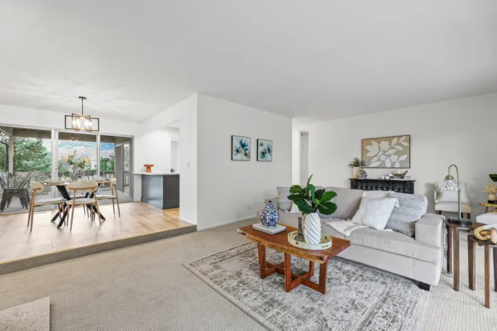 Carpeted living area with abundant natural light, wood-finish flooring in the dining space, a modern dining chandelier, and a built-in kitchen peninsula with a light-toned countertop