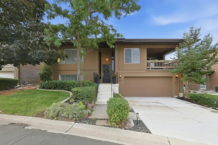 Split-level exterior with panel siding, an attached garage, a covered balcony, and mature landscaping