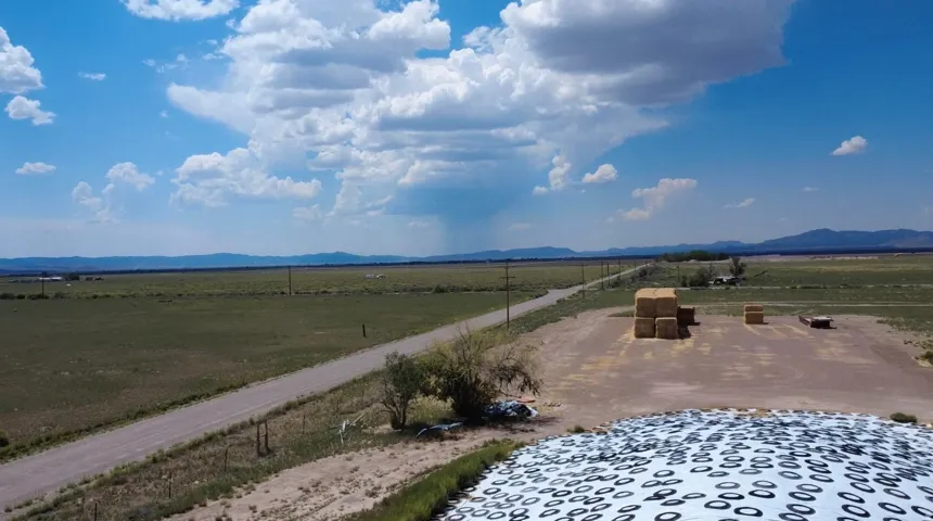 Expansive open land with a gravel road, distant mountains, and agricultural structures
