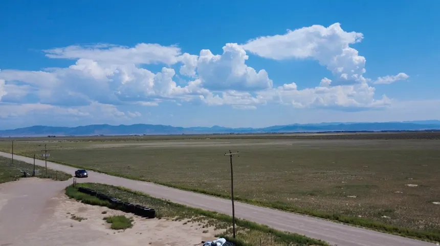 Expansive open land with a dirt road, distant mountains, and clear skies