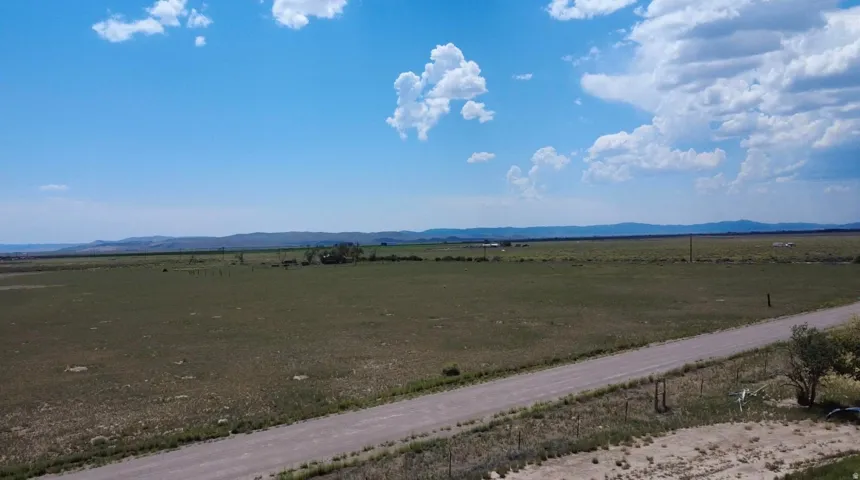 Expansive open land featuring a gravel road, distant mountain range, and scattered vegetation