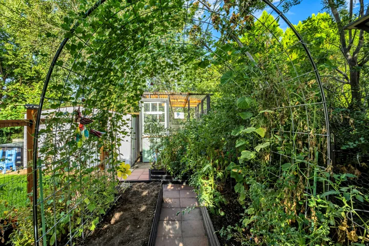 Garden archway with trellises, surrounded by lush foliage, leading to a potting shed with a windowed door