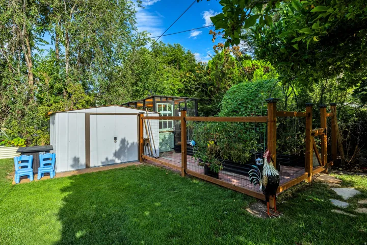Manicured lawn, a white storage shed, raised garden beds with wood fencing, and mature trees