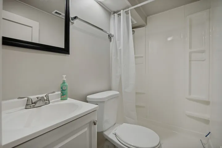Vanity with integrated sink, chrome faucet, wall-mounted mirror, and a shower/tub combination with built-in shelving