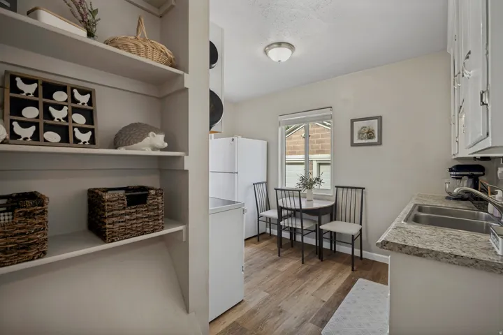 Built-in open shelving, wood-finish flooring, white cabinetry, double basin stainless steel sink, and light-toned countertops