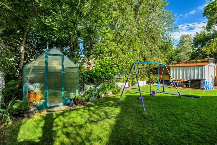 Expansive green lawn, mature trees, a clear-paneled greenhouse, and an outdoor storage shed