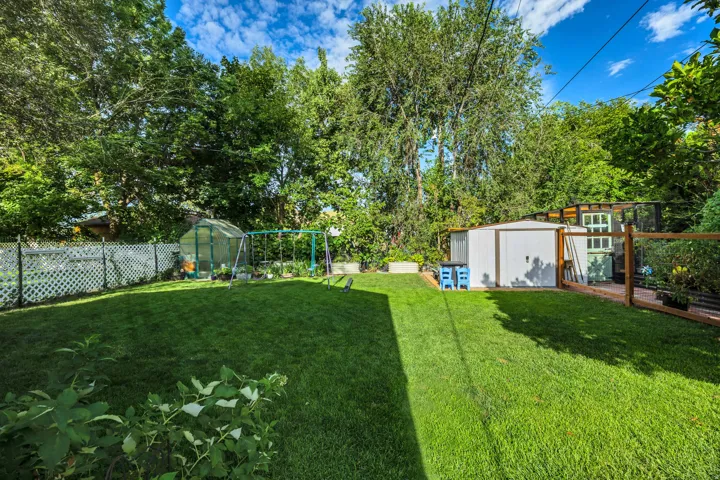 Expansive green lawn with a white lattice fence, a greenhouse structure, a storage shed, and mature trees