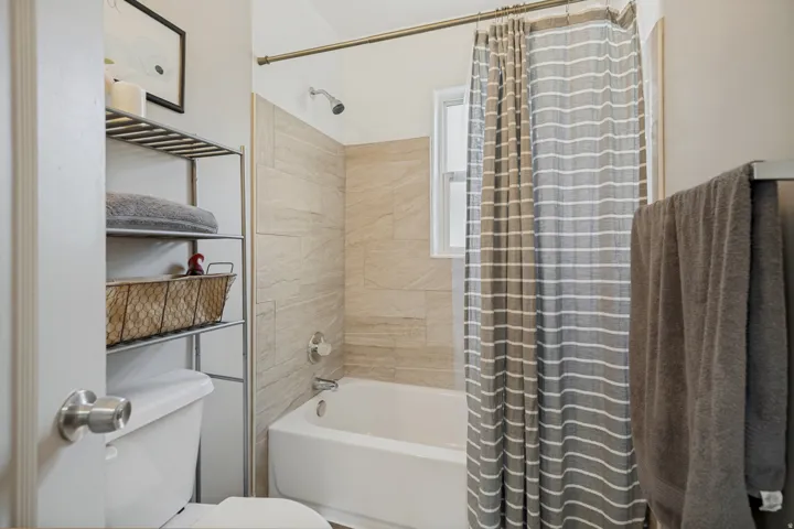 Bathtub with light-toned tiled surround, wall-mounted shower head, and window