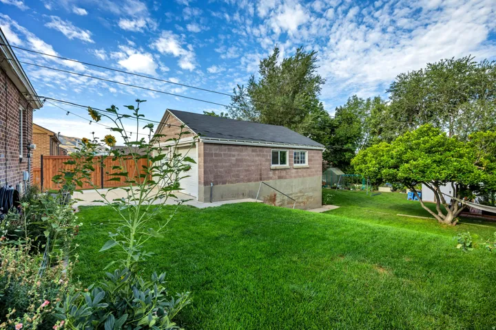 Detached garage with a roll-up door and side windows, surrounded by a large grassy area and mature trees