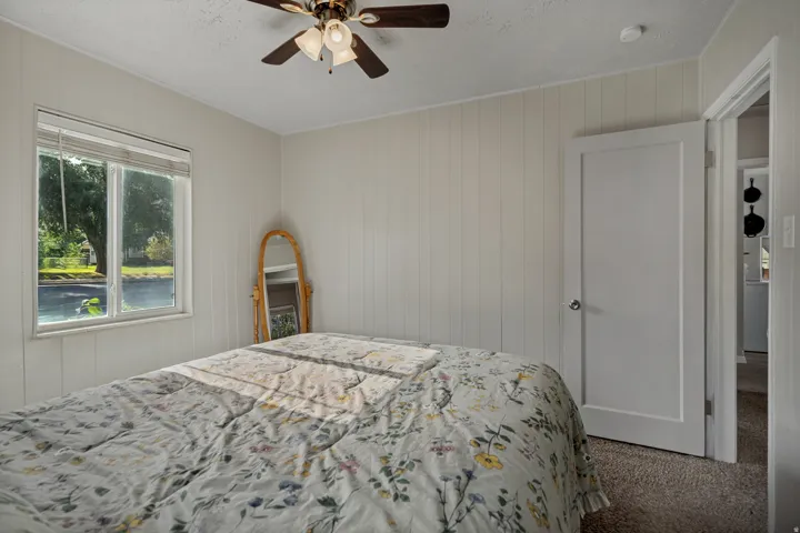 White paneled walls with a window, ceiling fan, and carpeted flooring