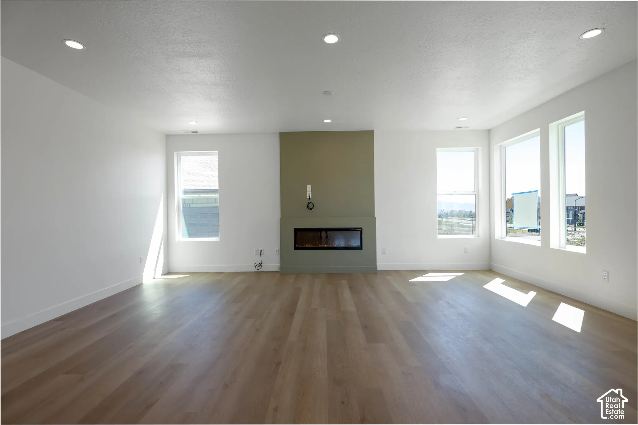 Spacious interior featuring a contemporary fireplace with a green accent wall, recessed lighting, expansive windows, and wood-finish flooring