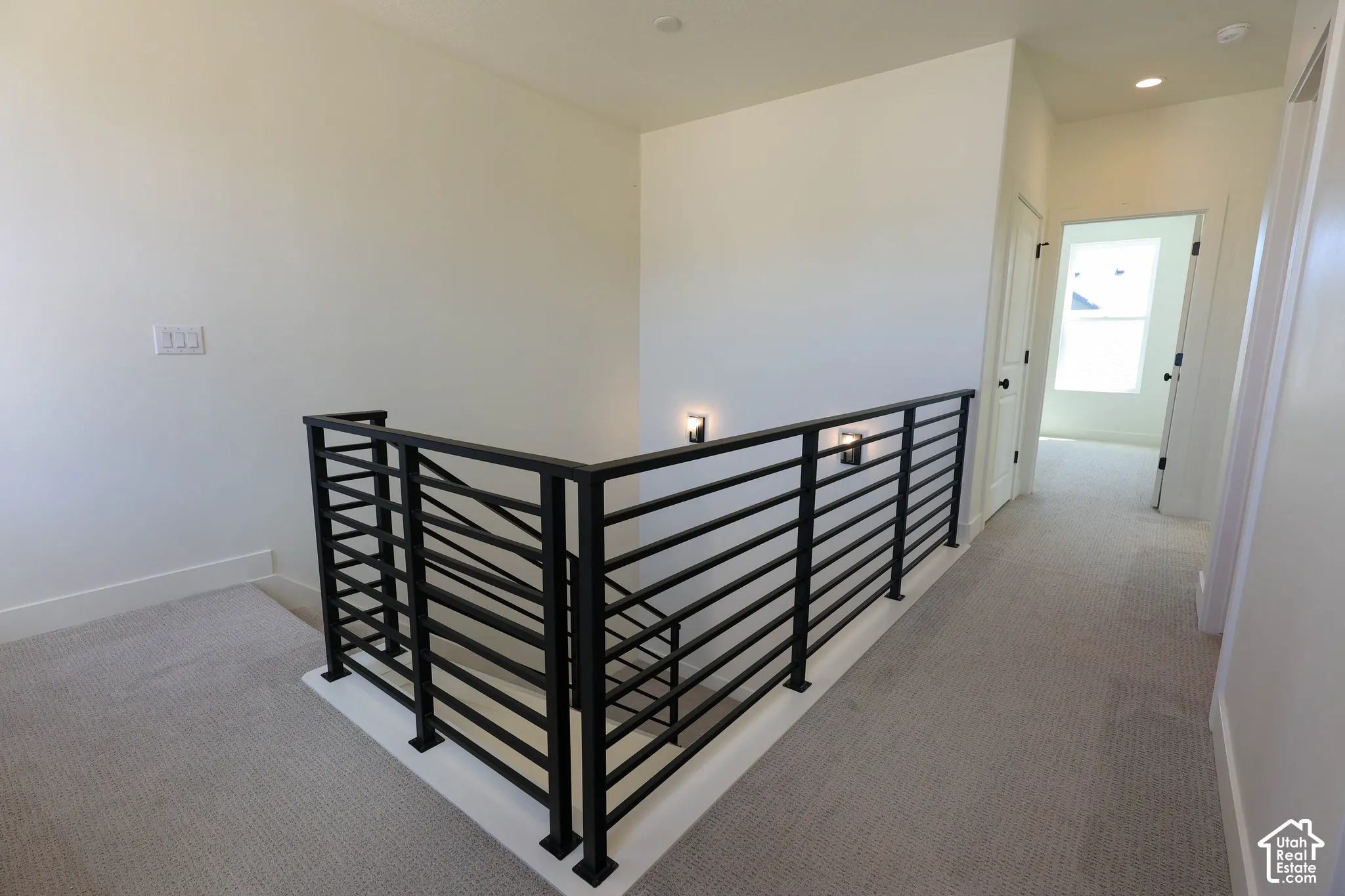 Modern metal stair railing with integrated wall sconces, neutral carpeting, and recessed lighting