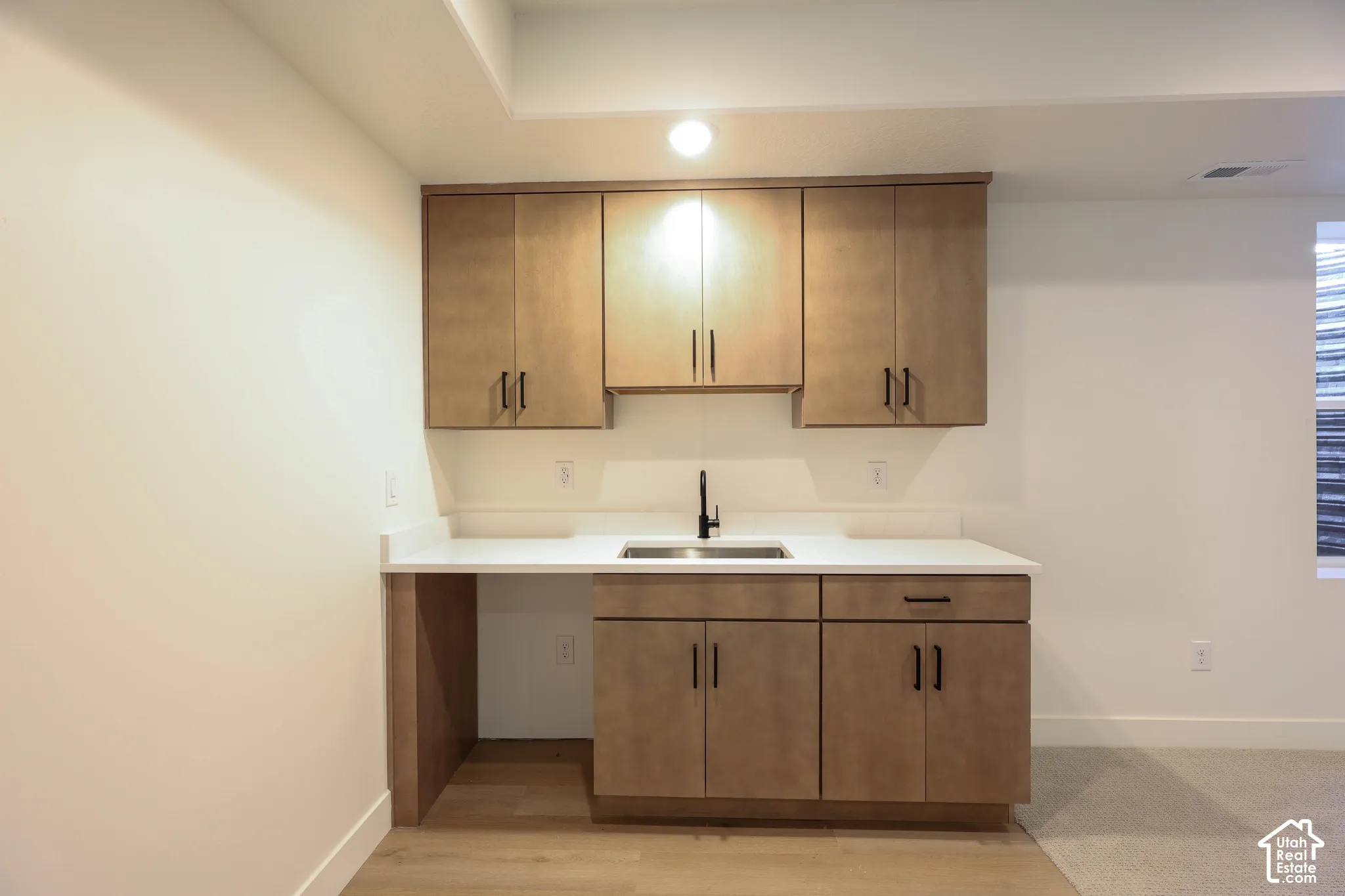 Newly finished wet bar featuring custom wood-finish cabinetry with brushed metal hardware, white quartz countertop, and stainless steel single-basin sink with modern faucet