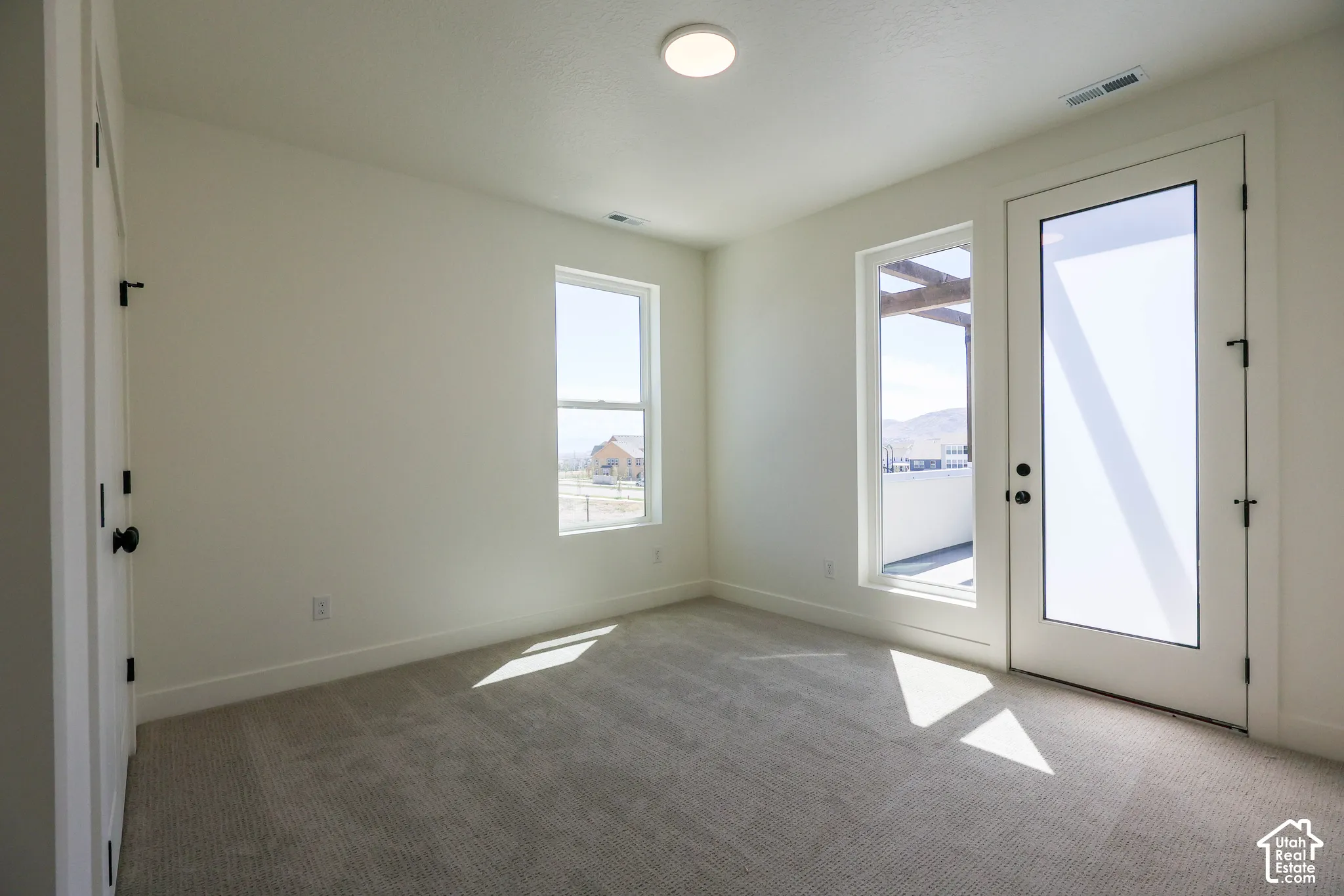 Bright, light-filled room with dual glass doors opening to exterior space, large picture window with natural sightlines, neutral wall finishes, and neutral-toned carpet flooring