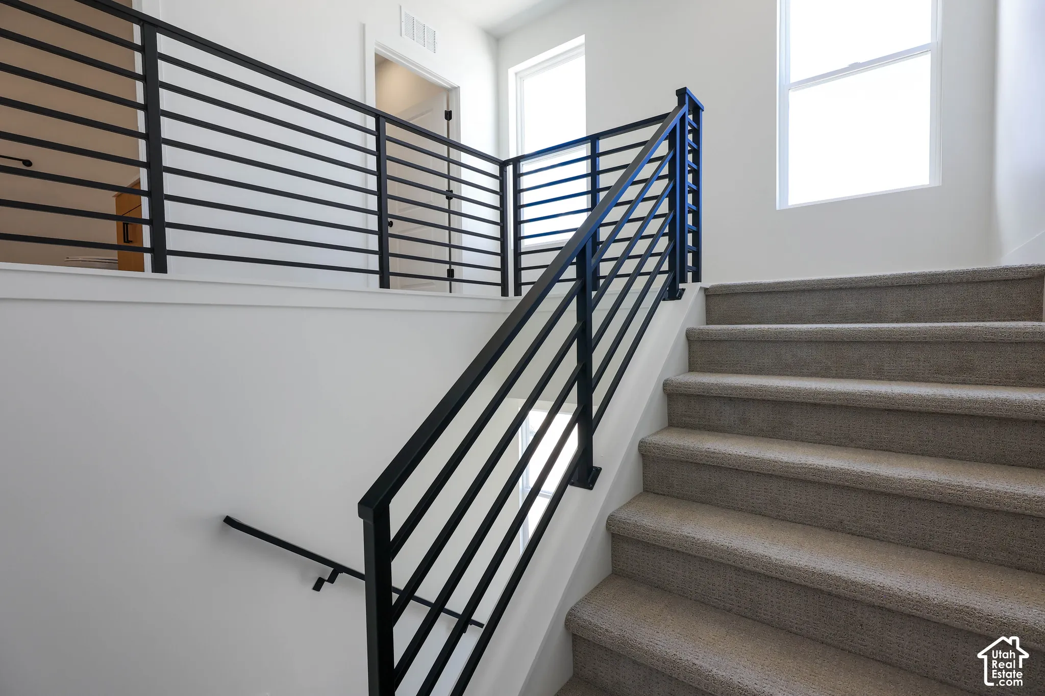 Staircase featuring carpeted treads, a black metal horizontal bar railing, and a coordinating handrail
