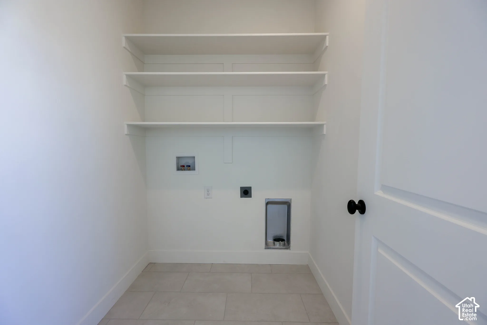 Upper level laundry room with White walls with integrated shelving, tile flooring, and a flat panel door with matte black hardware