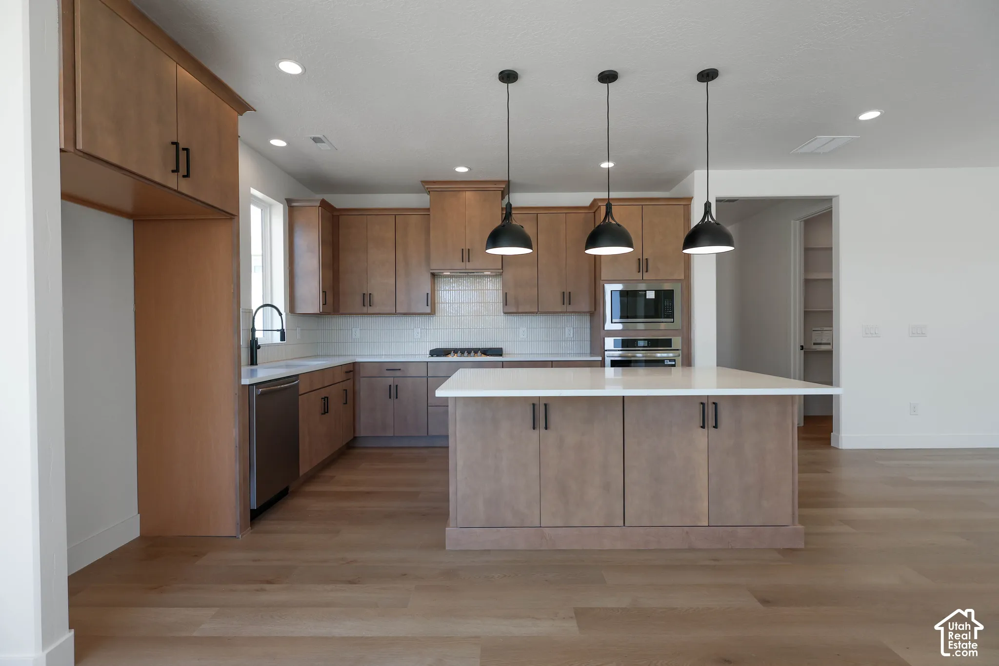 Kitchen featuring wood-finish cabinetry, stainless steel appliances, a white subway tile backsplash, and a large island with pendant lighting