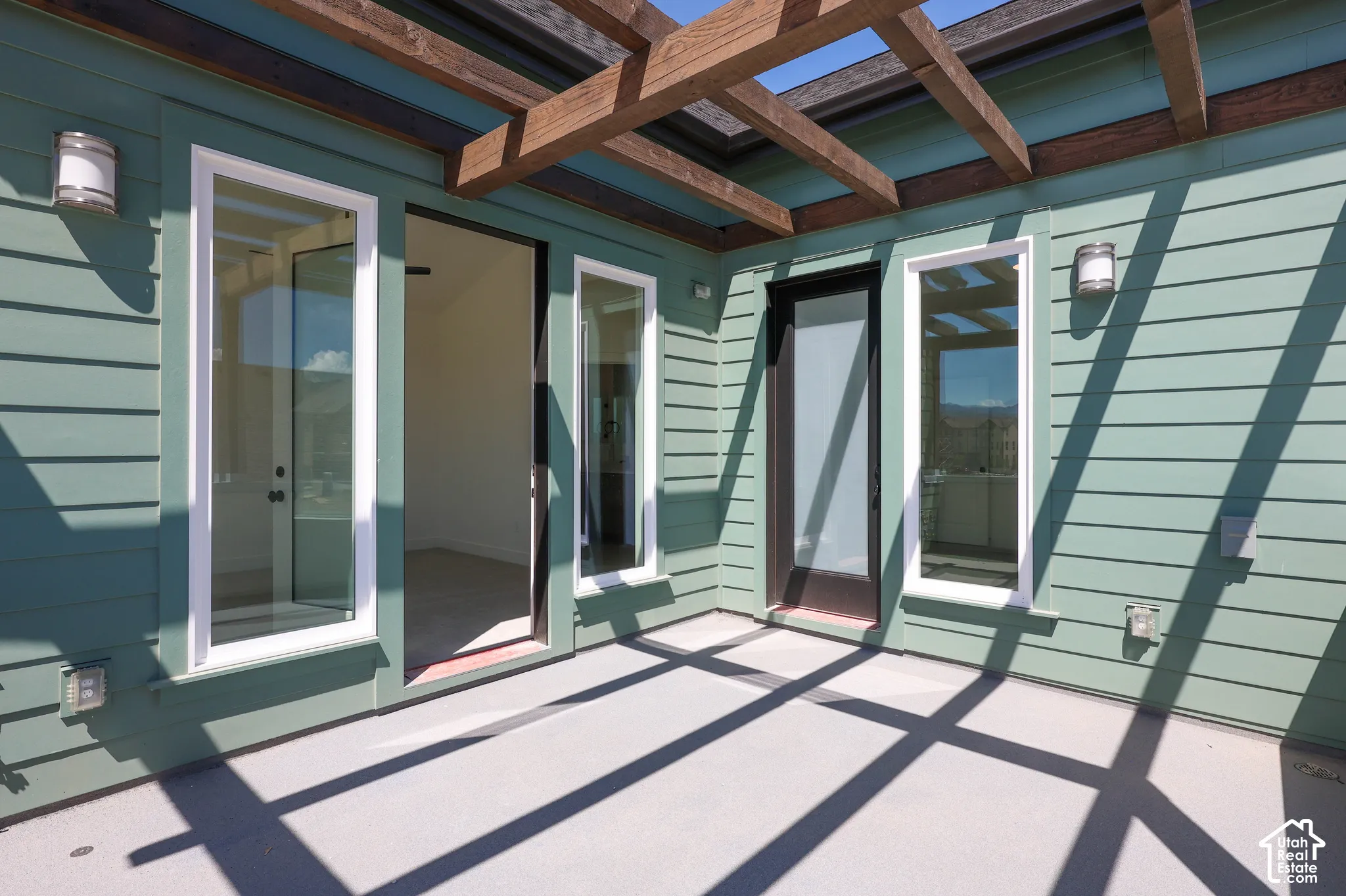 Outdoor balcony off of Primary bedroom with a wood pergola, horizontal plank siding, multiple glass-paned doors, and exterior wall sconces