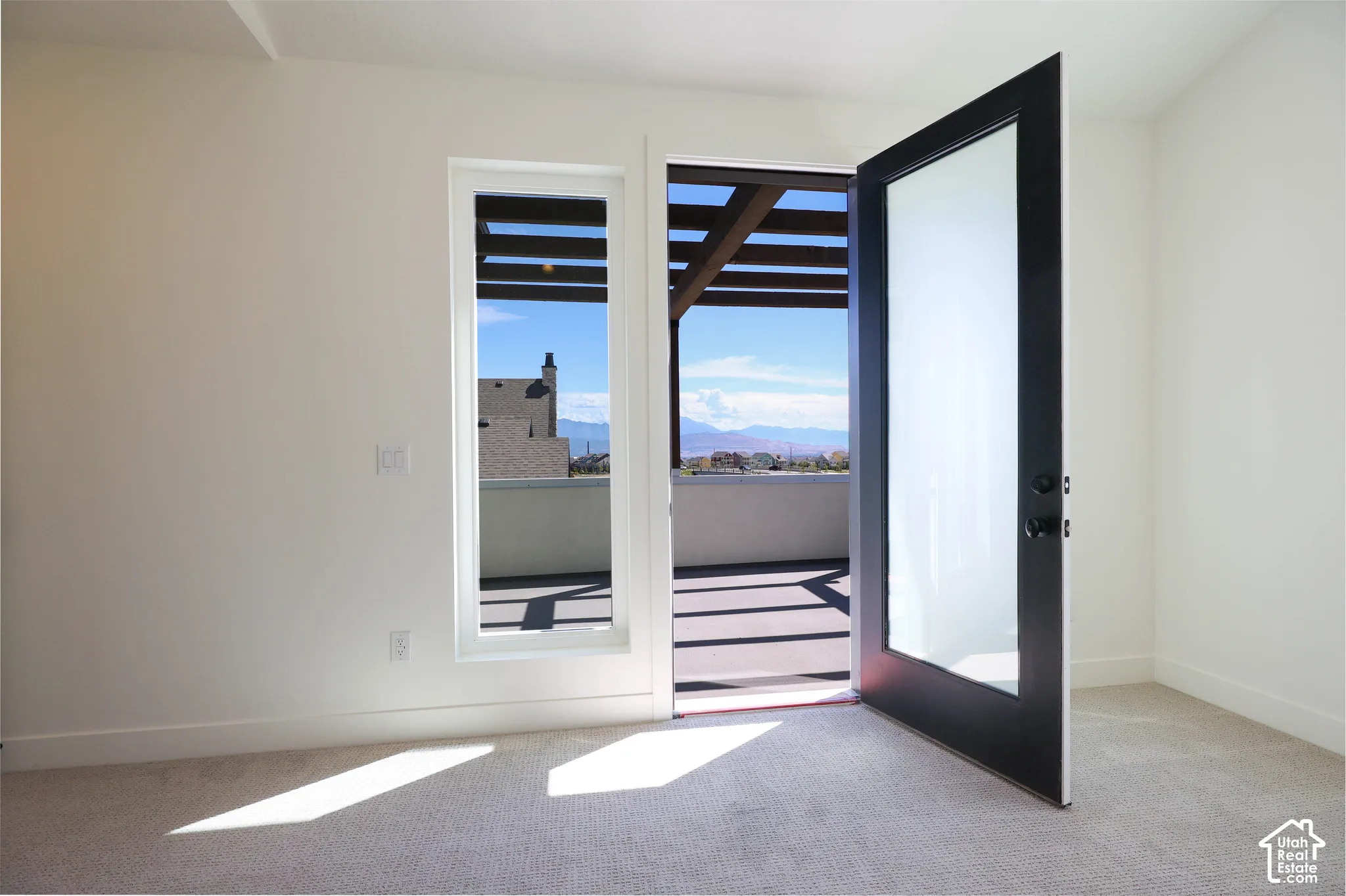 Primary bedroom with access to Balcony with wood pergola, accessible via a black-framed glass door, featuring neutral carpeting and a large window