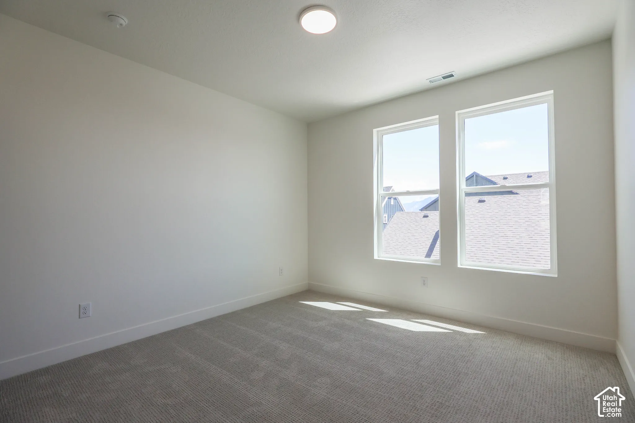 Spacious room featuring neutral carpeting, white walls, and a pair of large windows