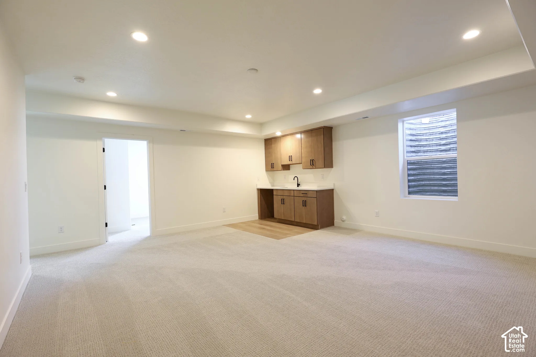 Recessed lighting, wood-finish cabinetry, white countertop, tile backsplash, and light-toned carpeting