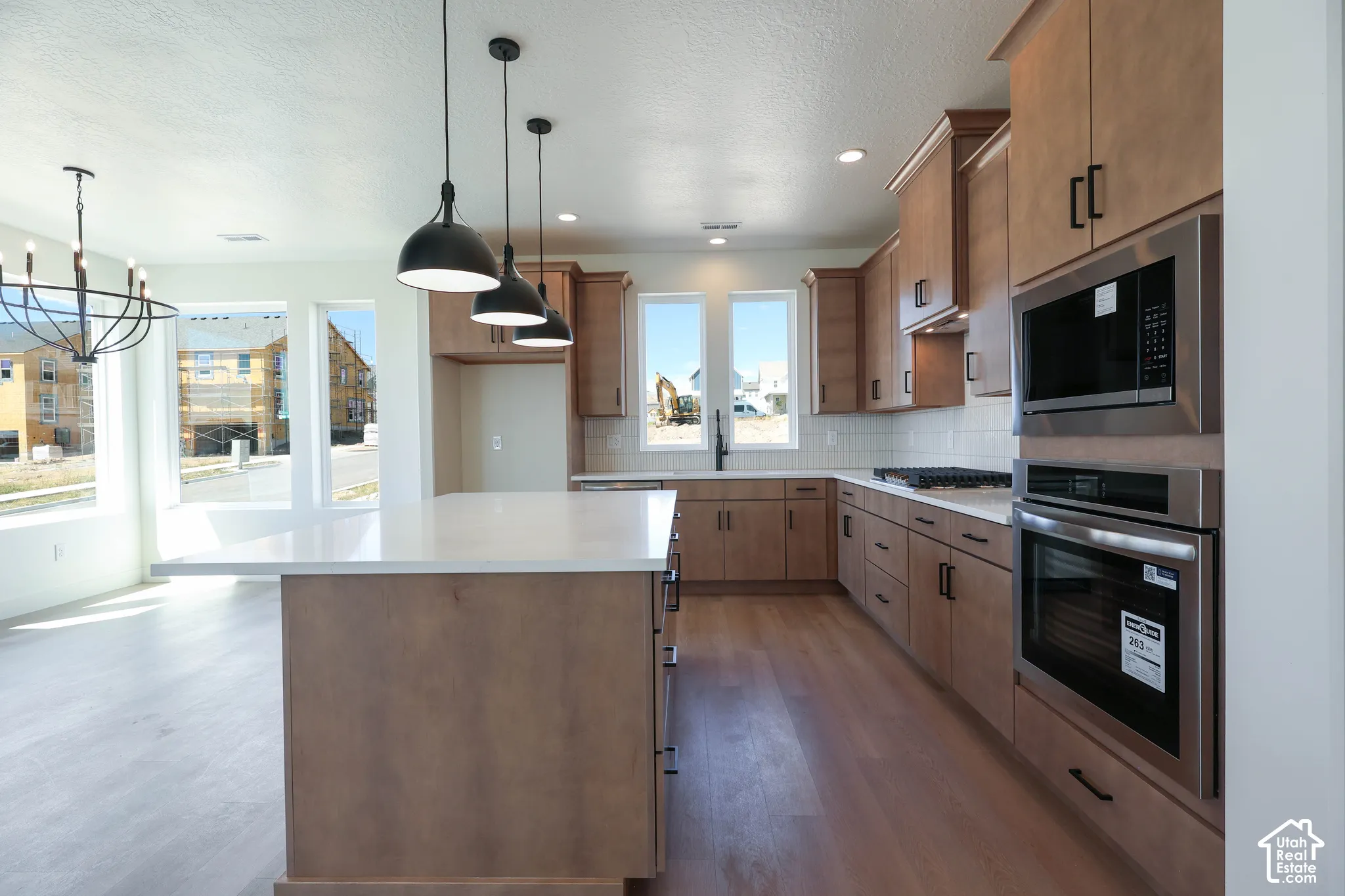 Spacious kitchen featuring an island with a light-toned countertop, a built-in oven and microwave, recessed lighting, and wood-finish flooring