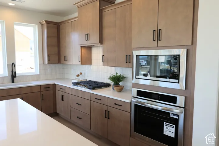 Light wood-finish cabinetry, stainless steel built-in appliances, white countertops, and a white subway tile backsplash