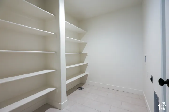 Basement laundry room with Built-in shelving, ample storage capacity, light-toned walls, and a tiled floor