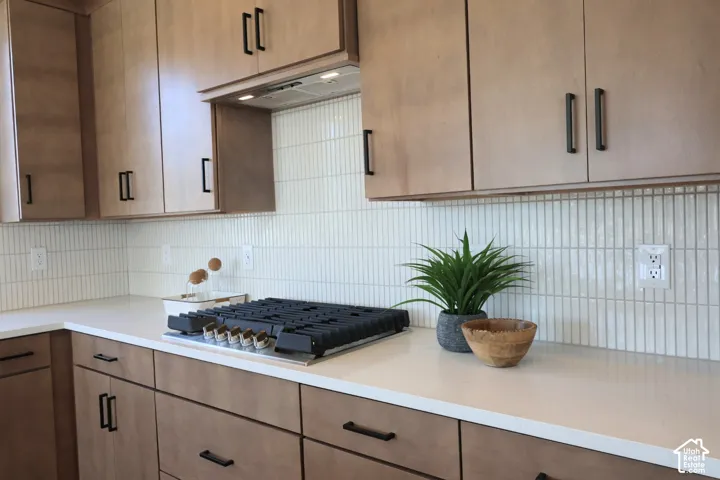 Wood-finish cabinetry with matte black hardware, integrated cooktop, white countertop, and vertical tile backsplash