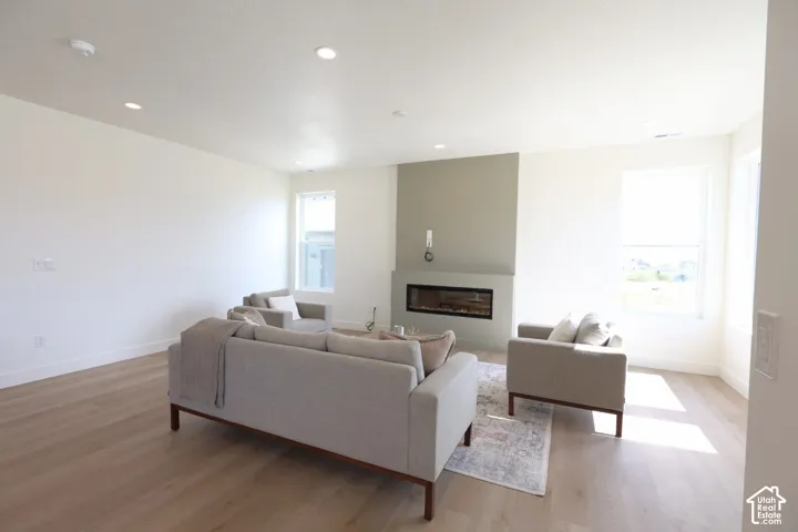 Spacious living area featuring wood-finish flooring, recessed lighting, expansive windows, a modern linear fireplace, and a light-toned accent wall