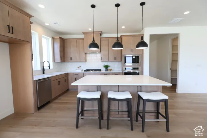 Modern kitchen featuring wood-finish cabinetry, stainless steel appliances, a center island with countertop, recessed lighting, and wood-finish flooring