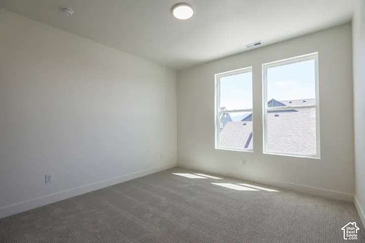 Spacious room featuring neutral carpeting, white walls, and a pair of large windows