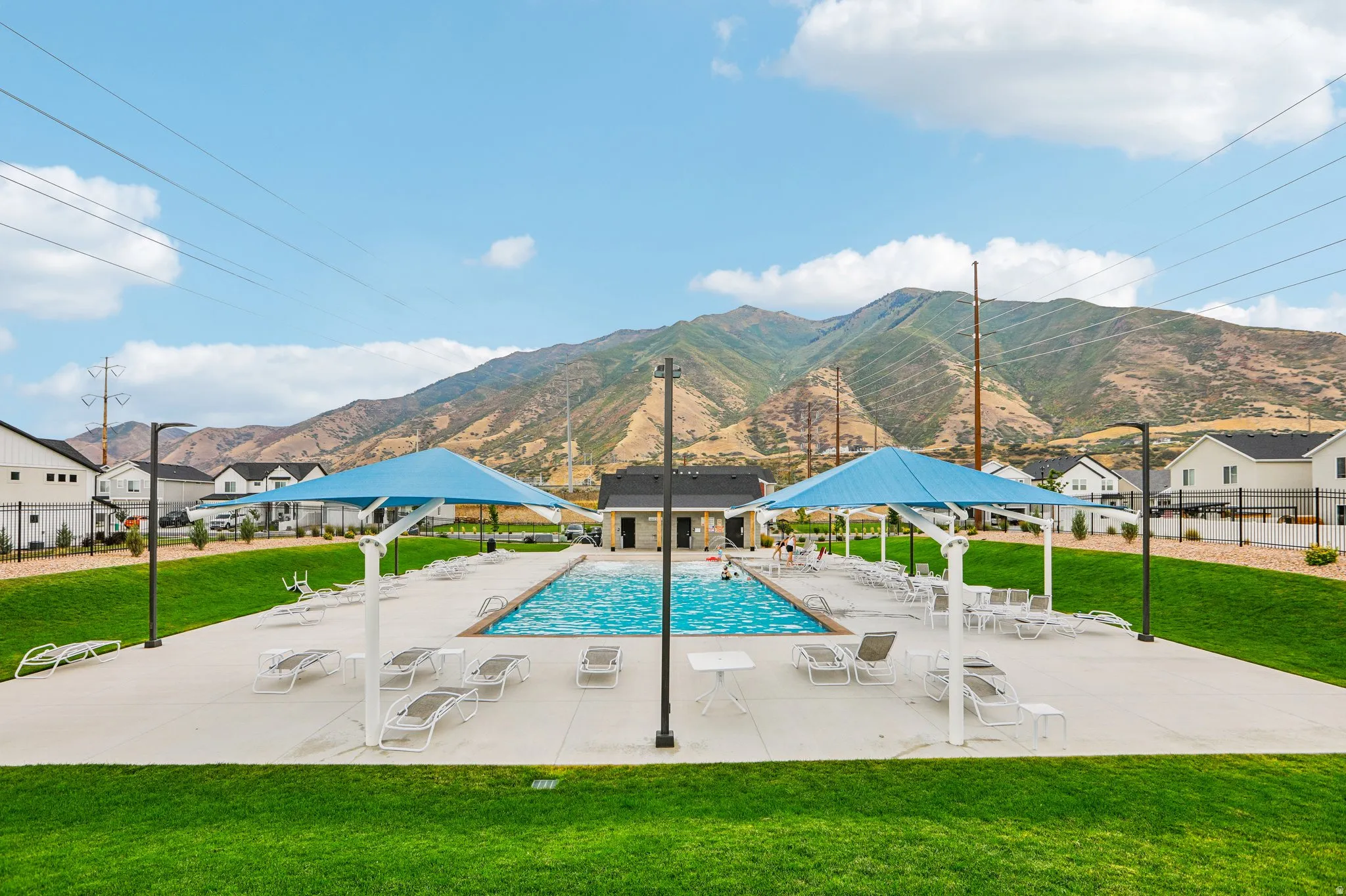 Outdoor swimming pool with a concrete deck, two blue shade structures, and a surrounding grass area